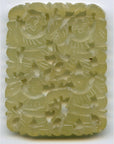 Close-up of green jade medallion, hand carved with four stylized figures, decorative patterns, and 2-inch metal bar.