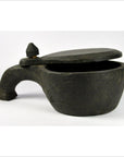 Close-up of round black clay mortar with a curved handle and sliding top, set against a white background.