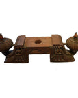Brown teak wood architectural element with ornate carved ends and central slot for sacred texts, close-up view.