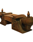 Brown teak wood carved architectural element with ornate side designs and two finials, intricate patterns visible.