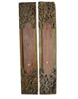 Close-up of two vertical brown wooden wall plaques with ornate hand-carved designs at the top and bottom.
