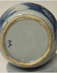 Close-up of hand painted blue and white Chinese ceramic vase with purple "M" mark and worn rim.