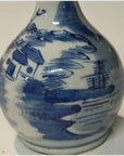 Blue and white ceramic Chinese vase with hand painted houses, water, and sailboat landscape scene, close-up view.