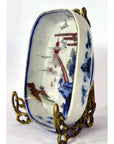 Close-up of blue and red hand painted Imari porcelain bowl on ornate gold metal stand, Asian-style landscape design.