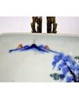 Close-up of hand painted Imari porcelain bowl with blue mountains, red trees, floral design, and brass hanger at top.