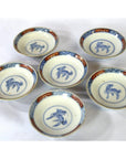 Set of six blue and white hand painted Imari porcelain small plates with animal designs and decorative borders on table.