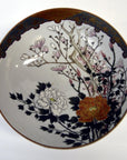White porcelain Kutani bowl with hand painted pink, orange, and white floral designs on dark branches, close-up.