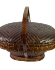 Close-up of dark and light brown rattan basket with chevron pattern, lid, and curved handle.