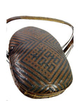 Brown-black rattan basket with curved handle and geometric diamond pattern, close-up on neutral background.