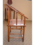 Side view of a wooden Horseshoe Chair with angled armrests on patterned carpet in a beige-walled room.