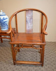 Brown wood Horseshoe Chair with rounded backrest beside a table holding a blue and white ceramic vase.