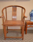 Dark wood horseshoe chair with curved backrest beside blue and white porcelain vase on wooden table.