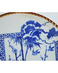Close-up of blue and white porcelain Igezara transferware plate with floral, bird, landscape motifs and iron-brown ridged edge.