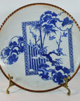White ceramic Igezara transferware plate with blue floral and bamboo motifs on a brass stand.