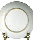 White Igezara transferware plate with gold rim on a metal stand, Meiji Period style, close-up view.
