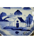 Blue and white porcelain Imari plate with hand painted house, trees, and fence scene, close-up view.
