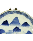 Blue and white ceramic Imari plate with hand-painted mountains, trees, and a patterned rim, close-up view.