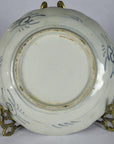 White ceramic Imari Japanese plate underside with blue hand-painted designs on a metal stand.
