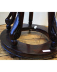 Close-up of antique dark brown lacquer incense stand with ornate curved legs on circular wood support, on wooden floor.