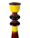 Close-up of a yellow, red, and black hand-carved wooden candlestick holder with rounded sections.