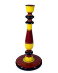 Close-up of tall, hand-carved wooden candlestick holder painted yellow, red, and black with a broad round base.