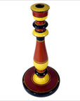 Close-up of tall, hand-carved wooden candlestick in red, yellow, and black folk art with round base.