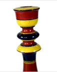 Close-up of a hand-carved wooden candlestick with red, yellow, and black folk art bands.
