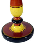 Close-up of red, yellow, and black painted rings on the hand-carved base of an India wood candlestick.