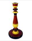 Close-up of a tall, hand-carved wooden candlestick in red, yellow, and black folk art style.