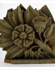 Brown hand carved wooden temple plaque with stylized floral and leaf motifs, weathered upper edge, close-up view.