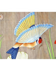 Colorful silk tapestry with bird showing light paint loss, among green plants and flowers.