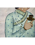 Close-up of a person’s torso and hand wearing multicolored silk tapestry, holding a decorated cup and saucer.
