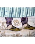 Close-up of patterned slippers on feet wearing purple leggings, resting on an India silk tapestry in very good condition.