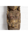 Close-up of polychrome hand carved wooden statue of Indian celestial musician against a white brick wall background.
