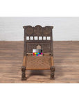 Brown wooden antique low seat chair with carved rosettes and rope seat, color calibration card on the seat.