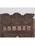 Close-up of a brown wooden Indian antique low seat chair with carved rosettes and woven rope seat.