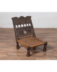 Brown wooden antique low seat chair with carved rosettes and rope seat on a wood floor.
