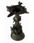 Close-up of dark brass Indian oil burner with intricate carvings and animal-shaped figures on the sides.