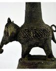 Close-up of a small, textured brass Indian oil burner next to a patterned collectible vase on a surface.