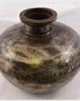 Close-up of a round, tarnished metal Indian water jug with wide neck on a plain background.