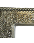 Close-up of silver-nickel Indian repoussé rectangular frame corner with embossed floral swirl detailing.