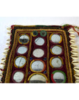 Close-up of multicolored hand sewn Indian cloth with circular mirrors, colorful thread, and cowrie shell accents.