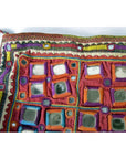 Close-up of a colorful embroidered Indian pouch with mirror accents and bright geometric patterns on fabric.