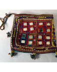 Colorful fabric square pouch with embroidery, mirror accents, braided strap, and tassels, close-up view.