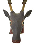 Close-up of a brown-and-yellow hand-carved Indonesian deer mask with large eyes, upright ears, and horns.