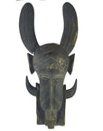 Brown wooden Indonesian hand carved figural shield with geometric carvings and tall curved horns, some visible cracks.