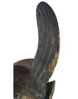 Close-up of a weathered brown wooden Indonesian hand-carved figural shield with visible curved lines and minor cracks.