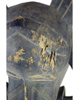Close-up of brown wooden Indonesian hand carved figural shield with geometric patterns, scratches, cracks, and repairs.