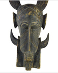 Brown wooden Indonesian hand carved figural shield with elongated features, horns, and geometric patterns on white background.
