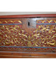 Brown wood Madura blanket chest with ornate gold floral and animal carvings, top keyhole, close-up view.